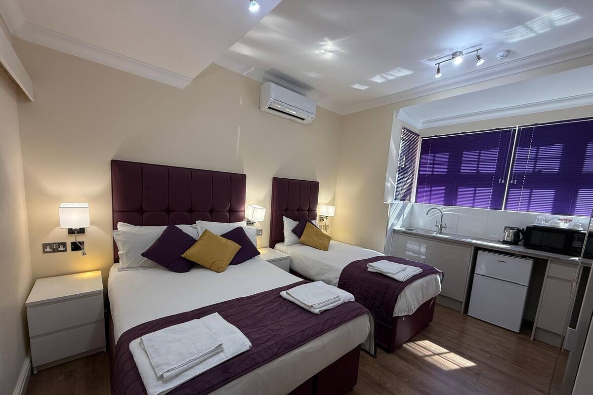 A hotel room with two beds, a small kitchenette, and a bathroom.