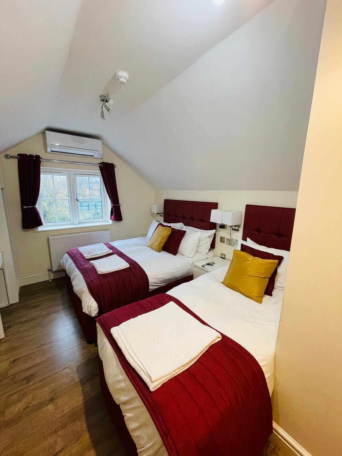 Une chambre avec deux lits, une fenêtre avec des rideaux, un appareil de climatisation et une table de chevet avec une lampe.