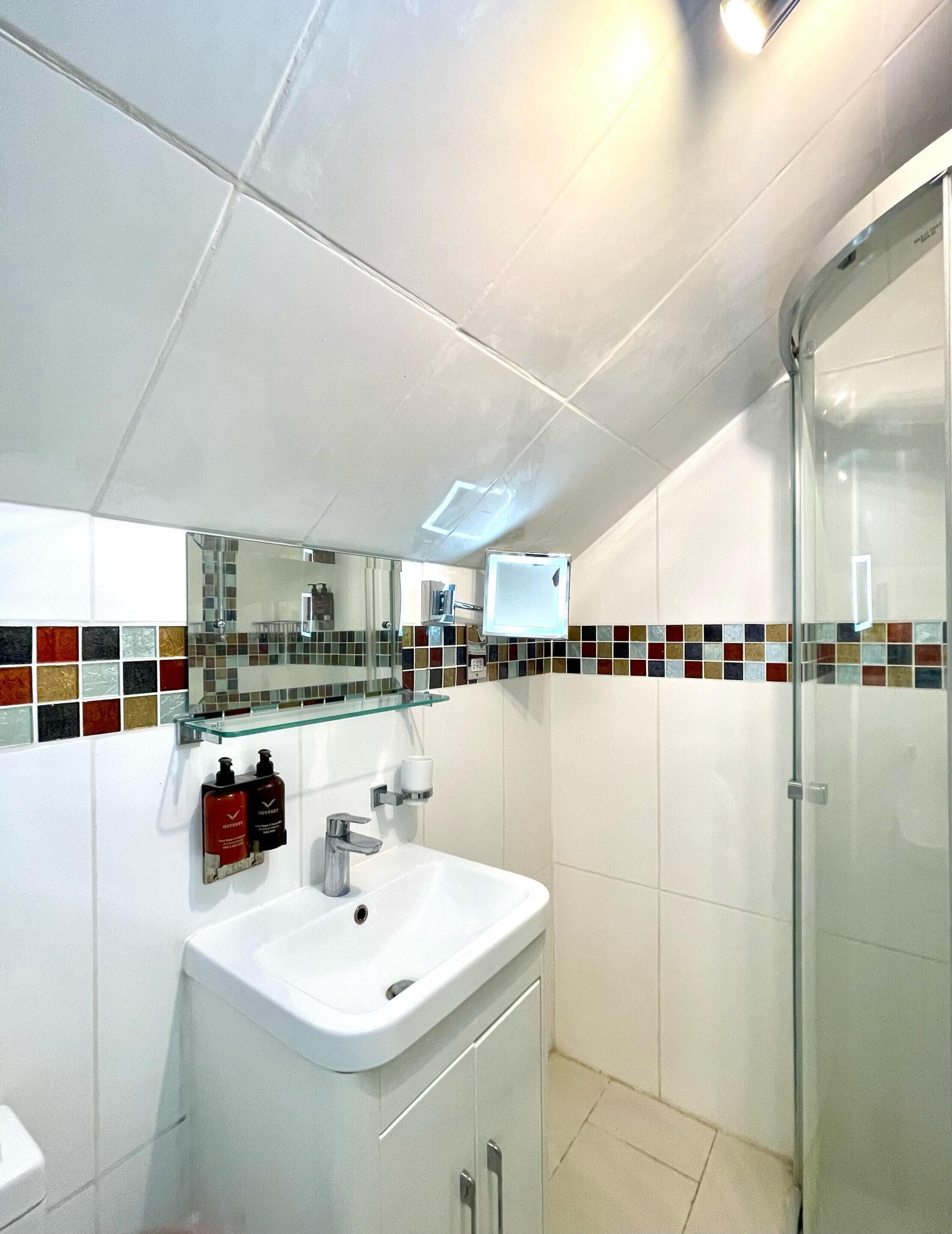 A modern bathroom with a white sink, glass shower enclosure, and a tiled backsplash.