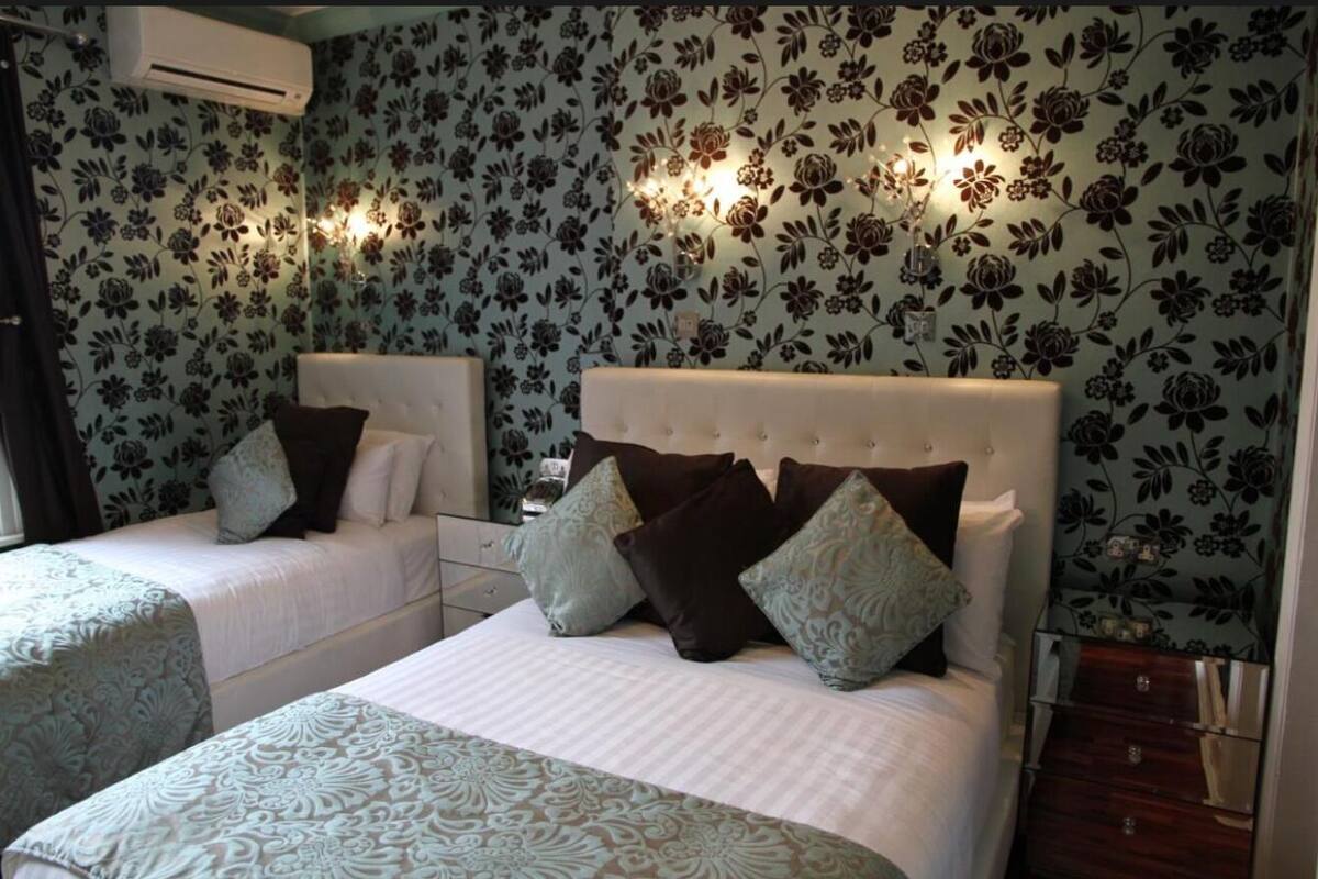 A hotel room with two beds, floral wallpaper, bedside lamps, and a dresser.