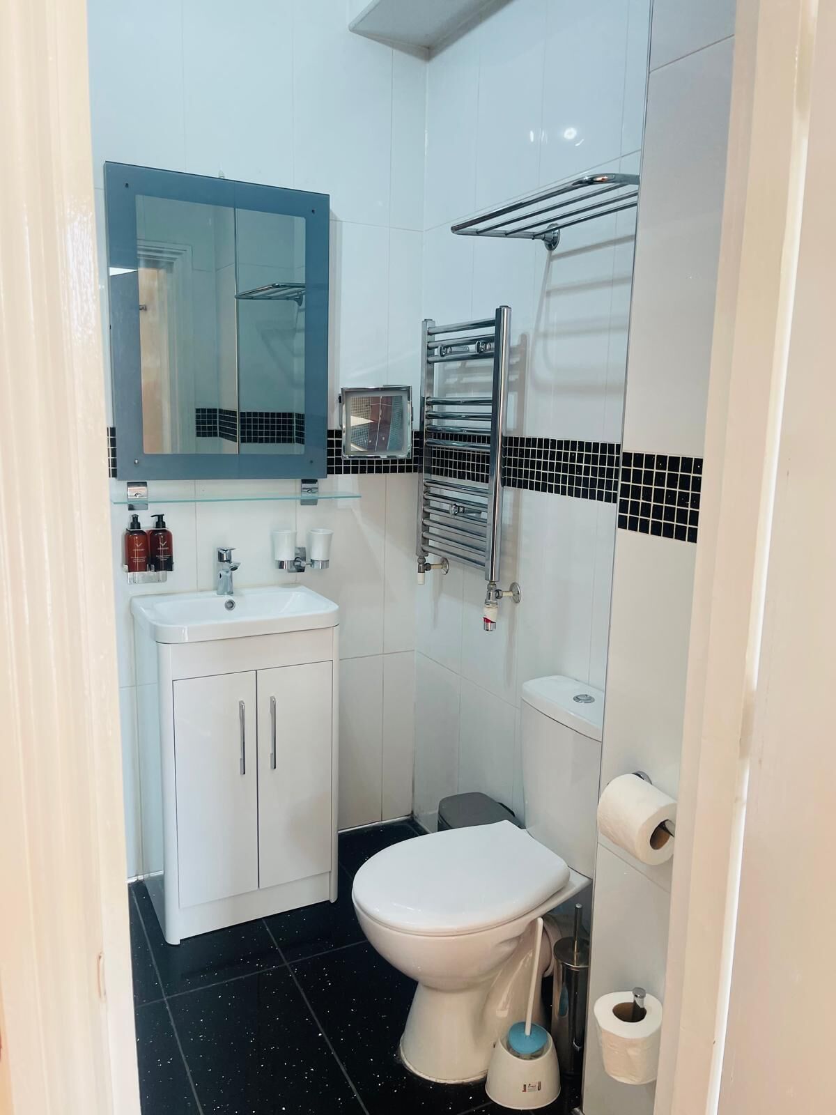 Une petite salle de bain avec des toilettes blanches, un lavabo surmonté d’un miroir et un porte-serviettes.