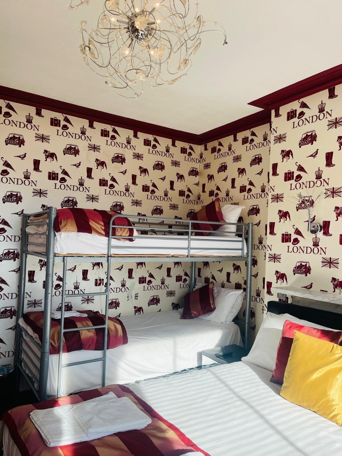 Une chambre avec des lits superposés, un lustre et un mur orné des lettres « LONDRES » et de divers motifs.