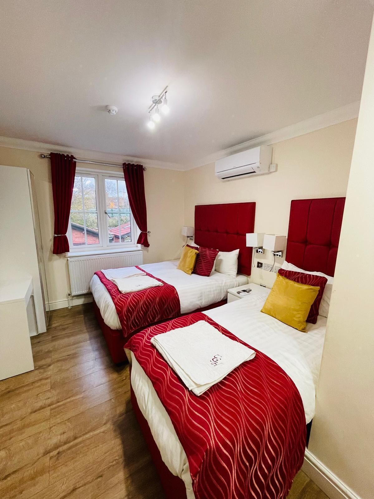 A hotel room with two beds, red headboards, white bedding, and a window with red curtains.