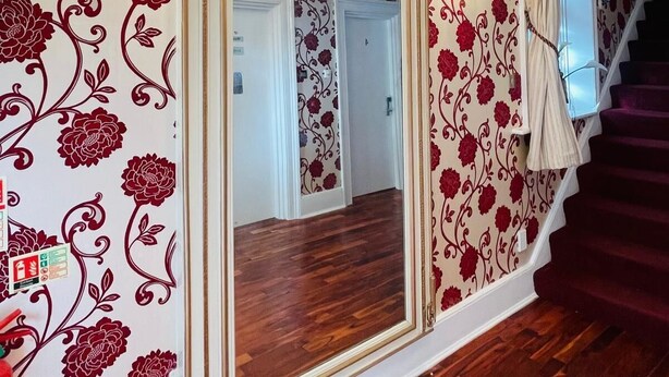 Una escalera con alfombra roja, un espejo con marco dorado y papel tapiz floral.