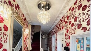 Un pasillo con papel tapiz estampado, un candelabro, una escalera y un radiador.