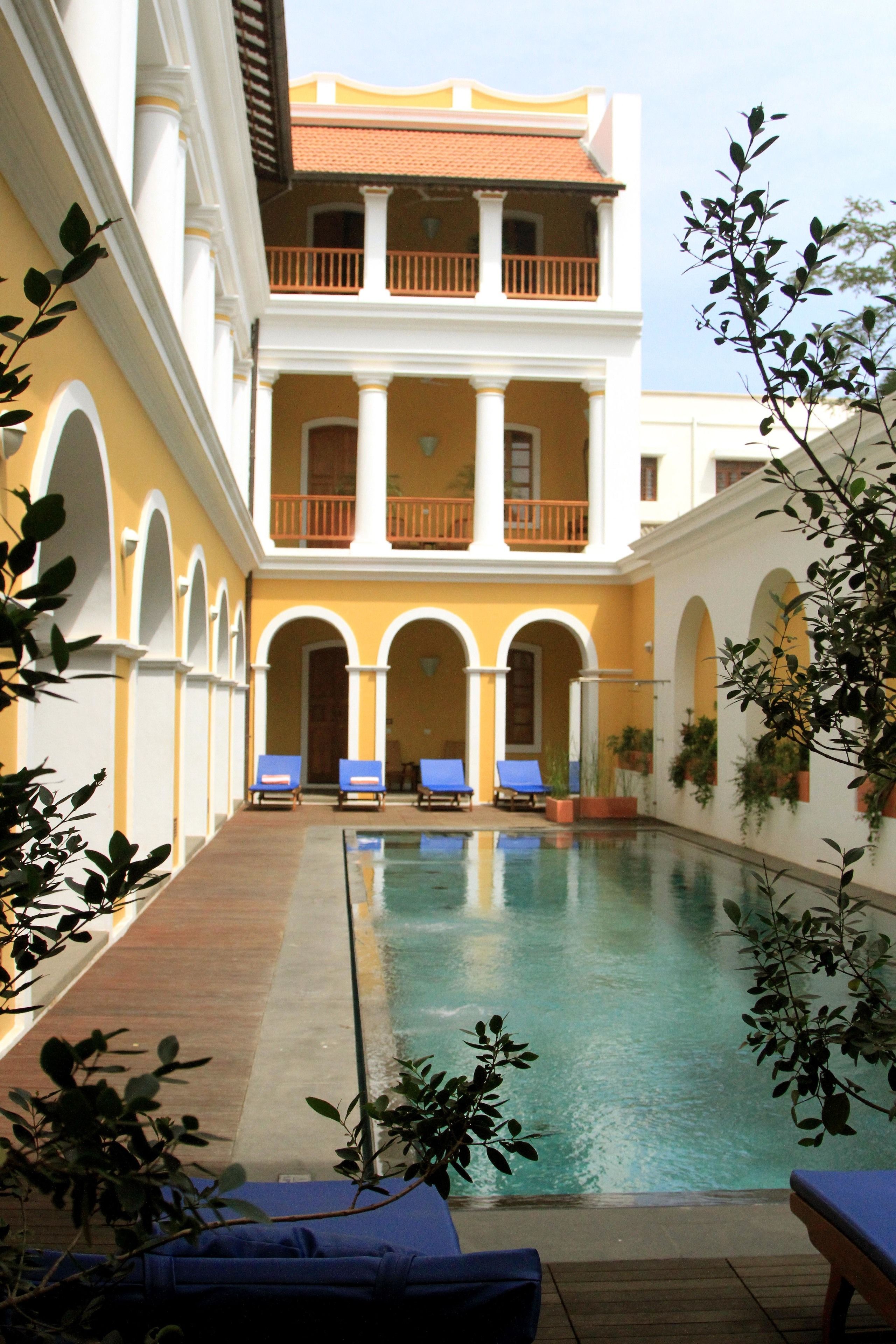 Un espace piscine avec des chaises longues, un bâtiment à deux étages doté de balcons et des portes en arc de cercle.