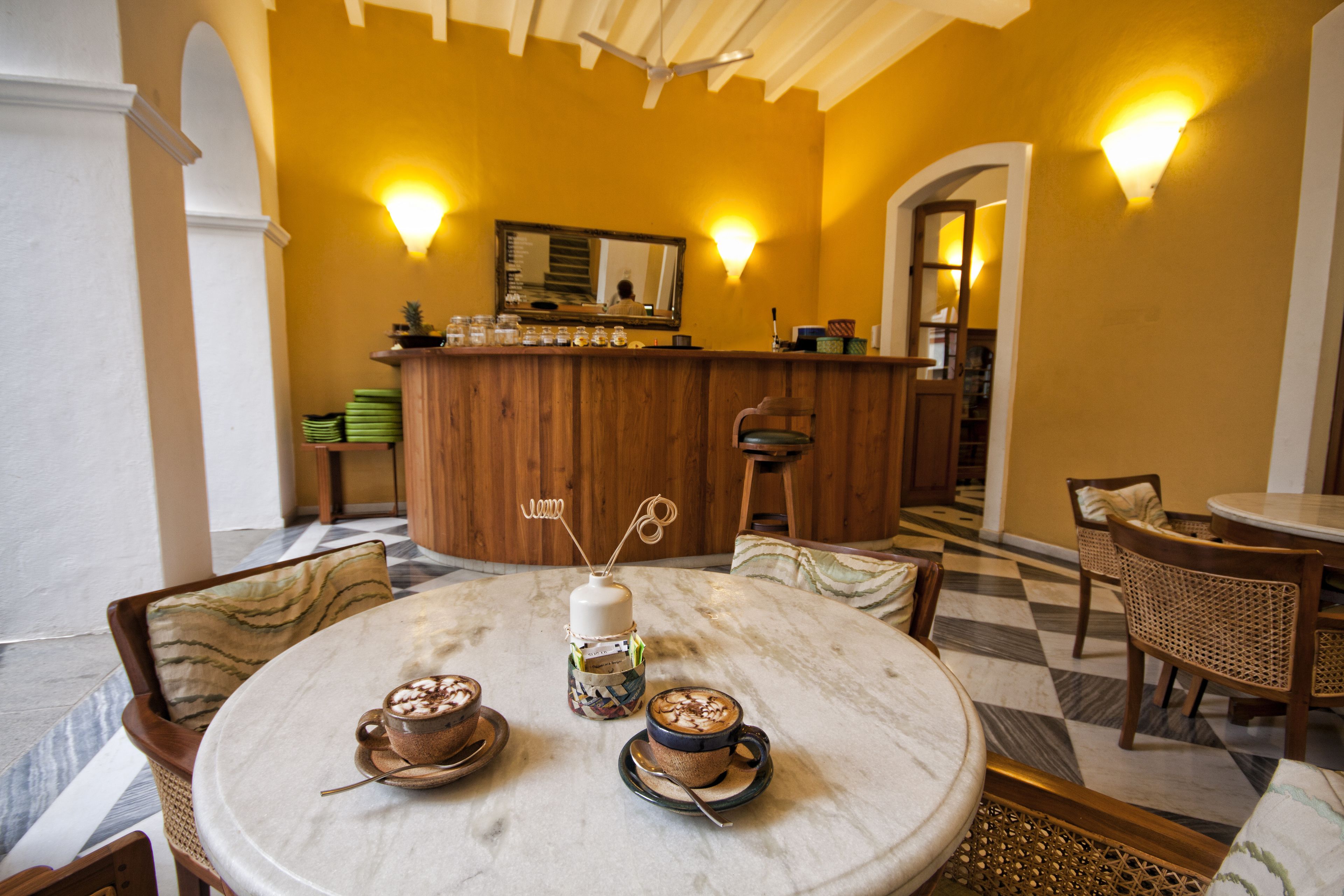 A round table with two coffee cups and a bottle, a wooden bar with a mirror, and a checkered floor.