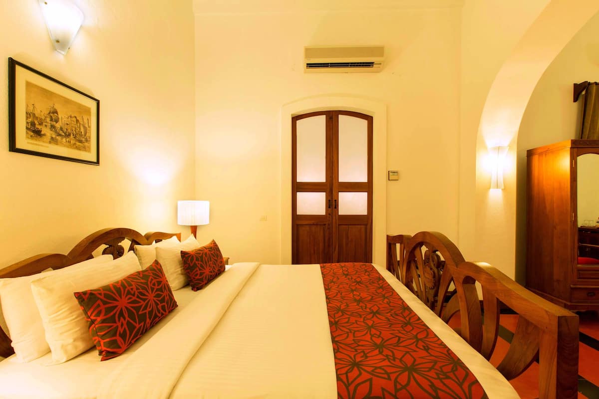 Une chambre d’hôtel avec un lit, une chaise en bois, un bureau et une porte dont les panneaux sont en verre dépoli.
