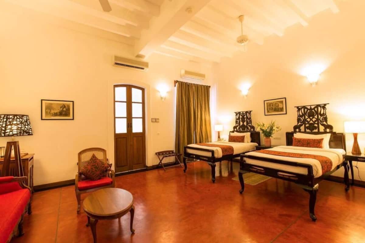 Une chambre d’hôtel avec un plancher en bois, deux lits, un canapé rouge, une petite table et une porte.