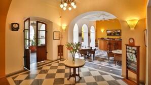 Un hall d’hôtel avec un sol à carreaux, une table ronde ornée d’un vase de fleurs et un coin bar avec des tabourets et un téléviseur.
