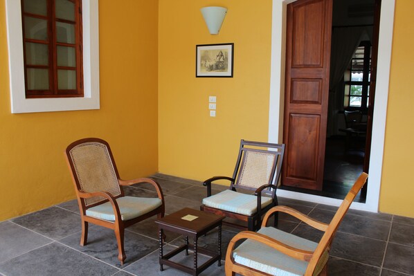 A room with two wooden chairs, a small table, and a picture on the wall. - Palais de Mahé - Cgh Earth (Puducherry)