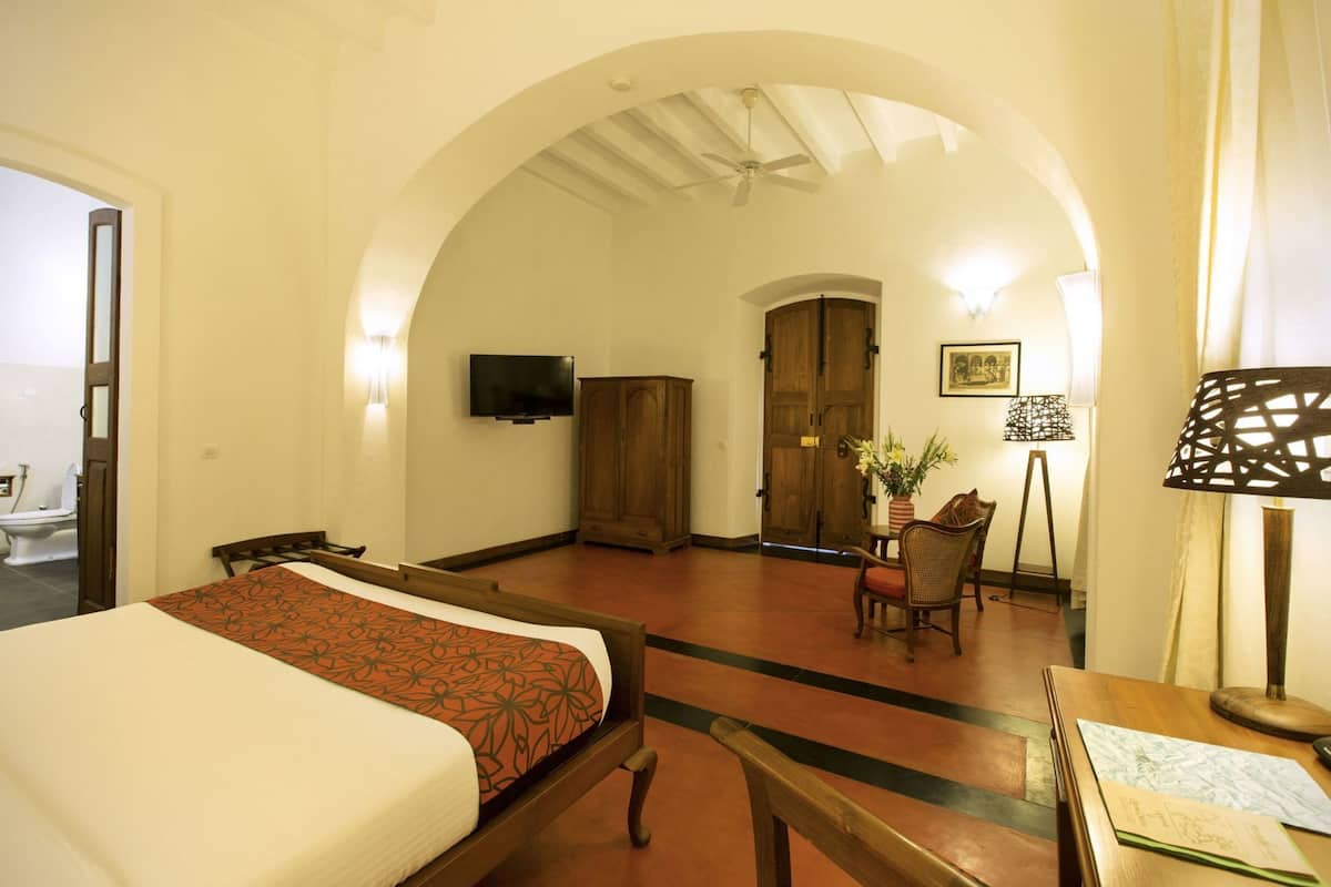 Une chambre d’hôtel comprenant un lit, un bureau, une chaise, une télévision, une armoire et un plafond en arc de cercle.