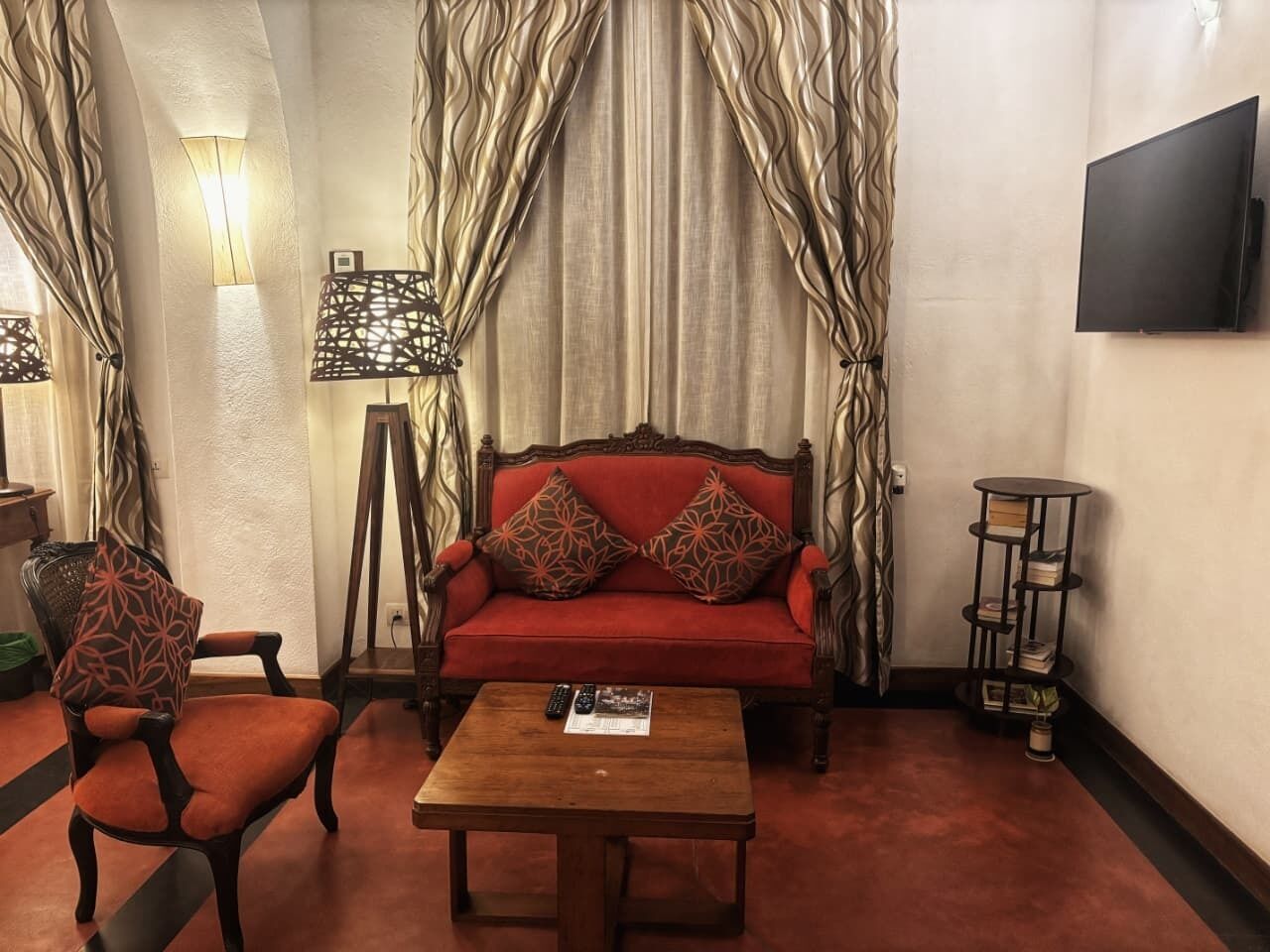 A room with a red sofa, a wooden coffee table, a patterned armchair, and a bookshelf.