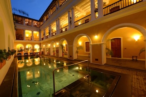 A multi-level hotel with a central swimming pool, multiple balconies, and warm lighting. - Palais de Mahé - Cgh Earth (Puducherry)