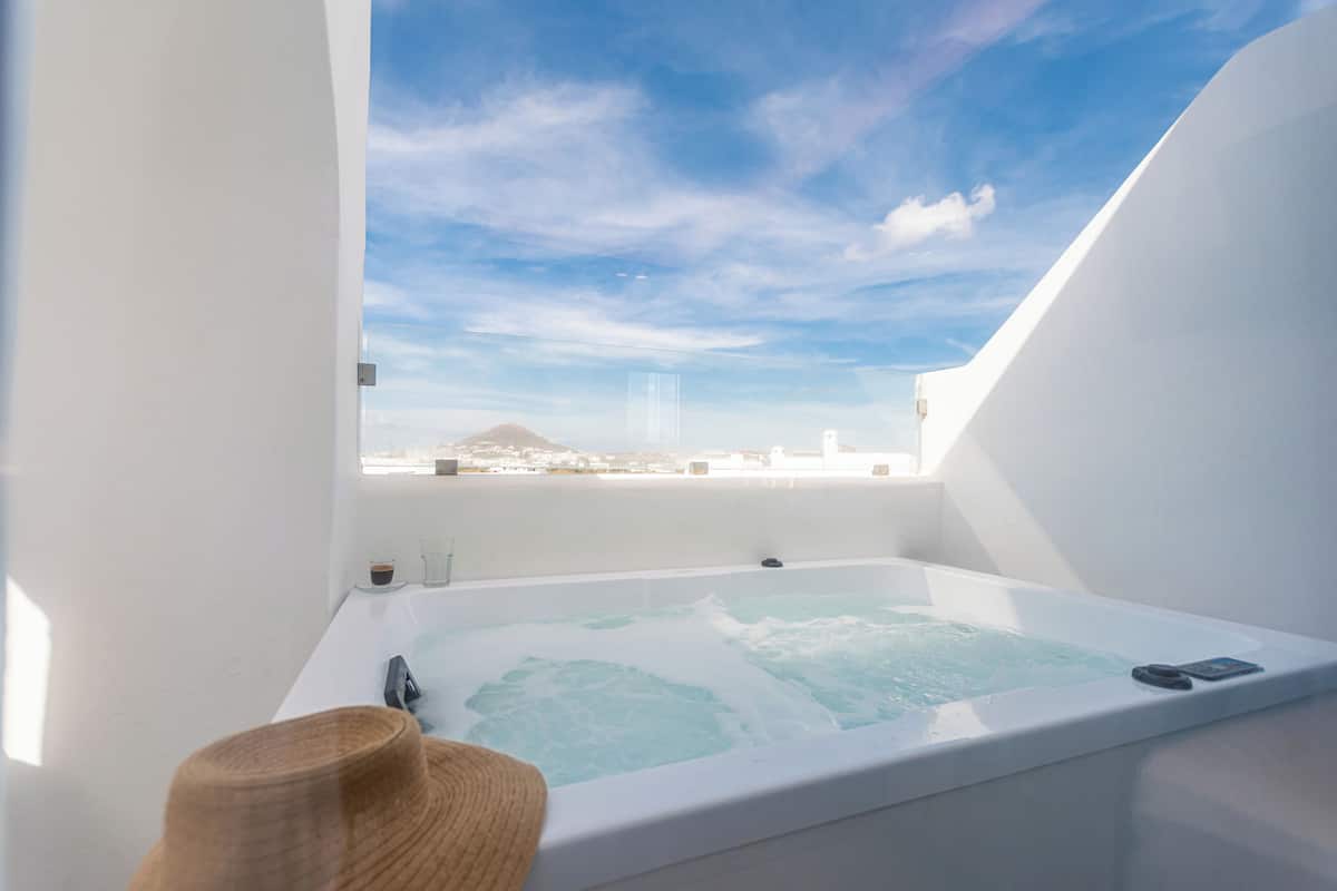 Ein modernes Badezimmer mit einer großen Badewanne, einem Fenster mit Blick auf die Stadt und einem Strohhut auf dem Boden.