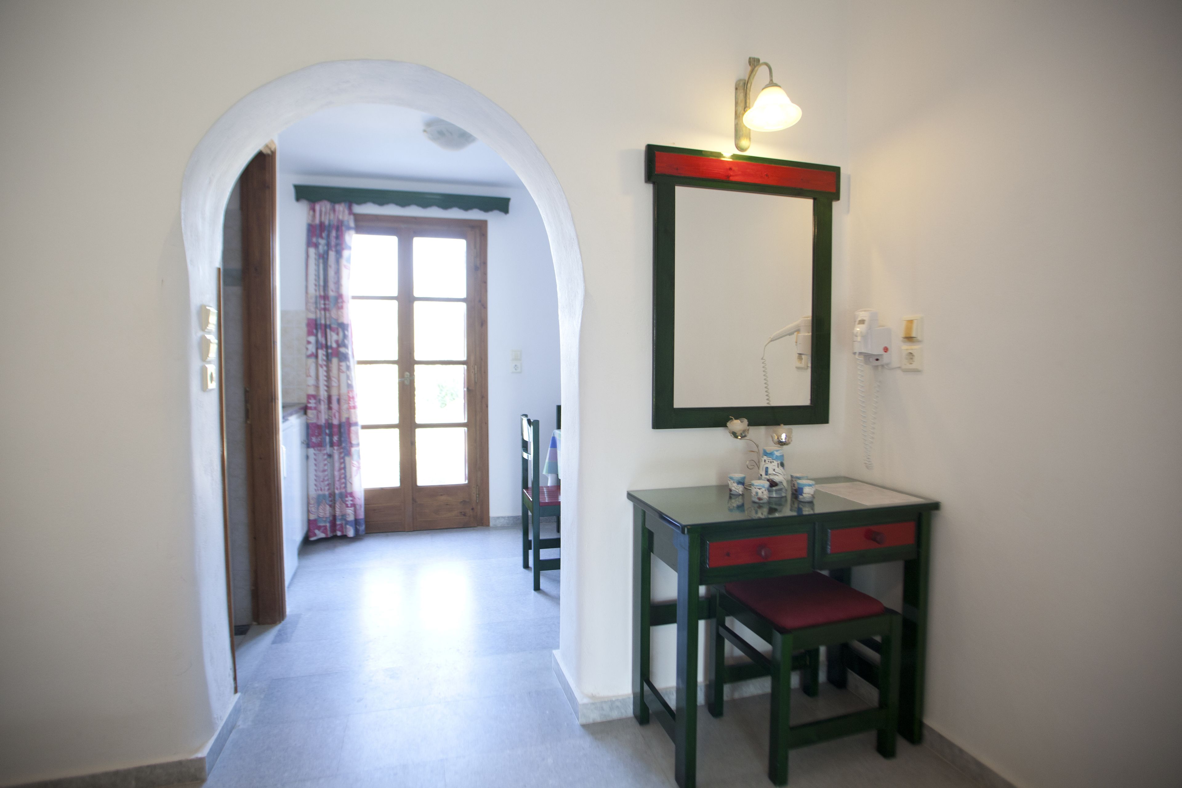 A narrow hallway with a wooden door, a small table with a mirror, and a chair.
