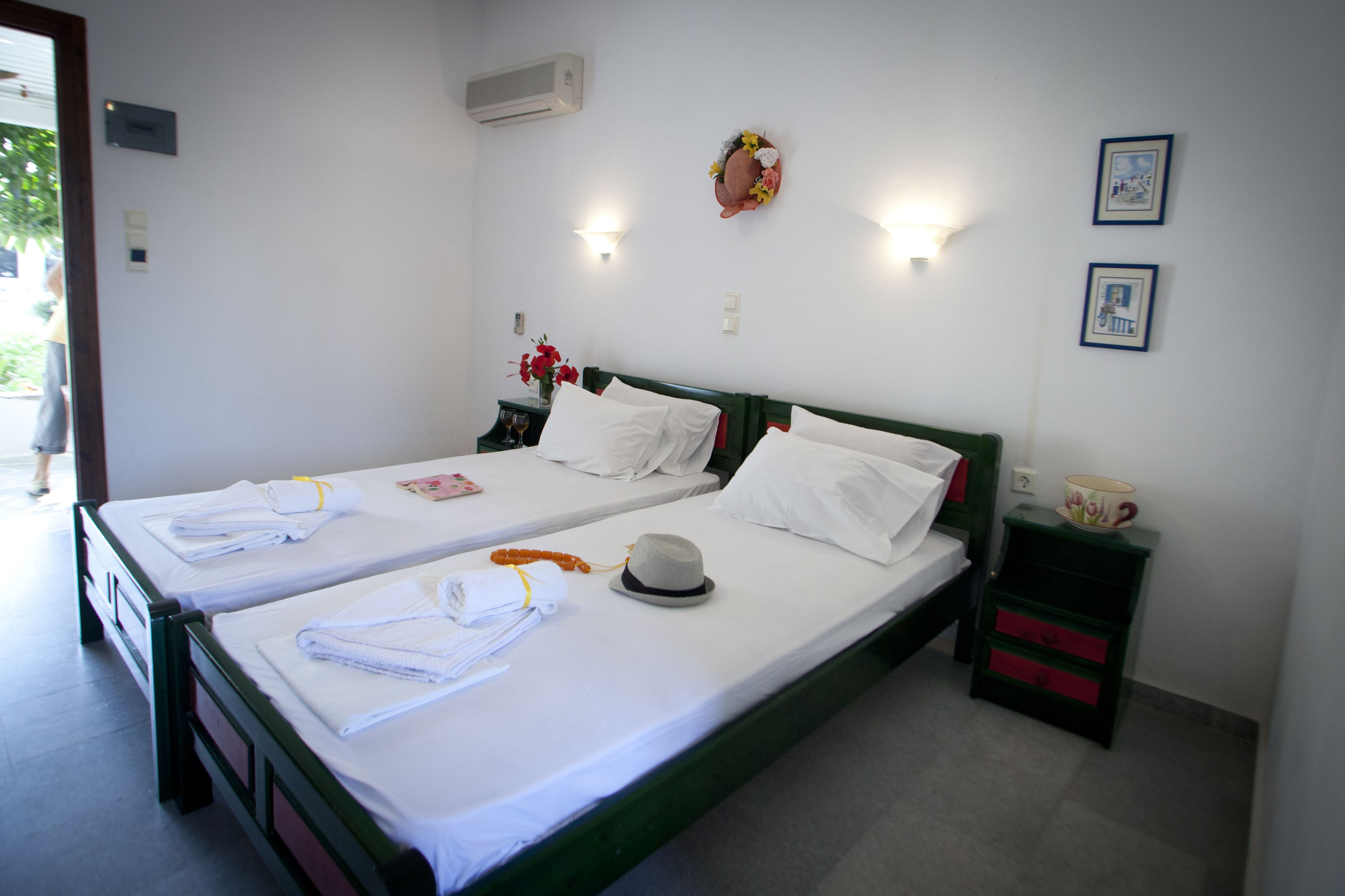 Hotelkamer met twee enkele bedden, een nachtkastje met een kopje en een kleine plant, en een wandairconditioner.