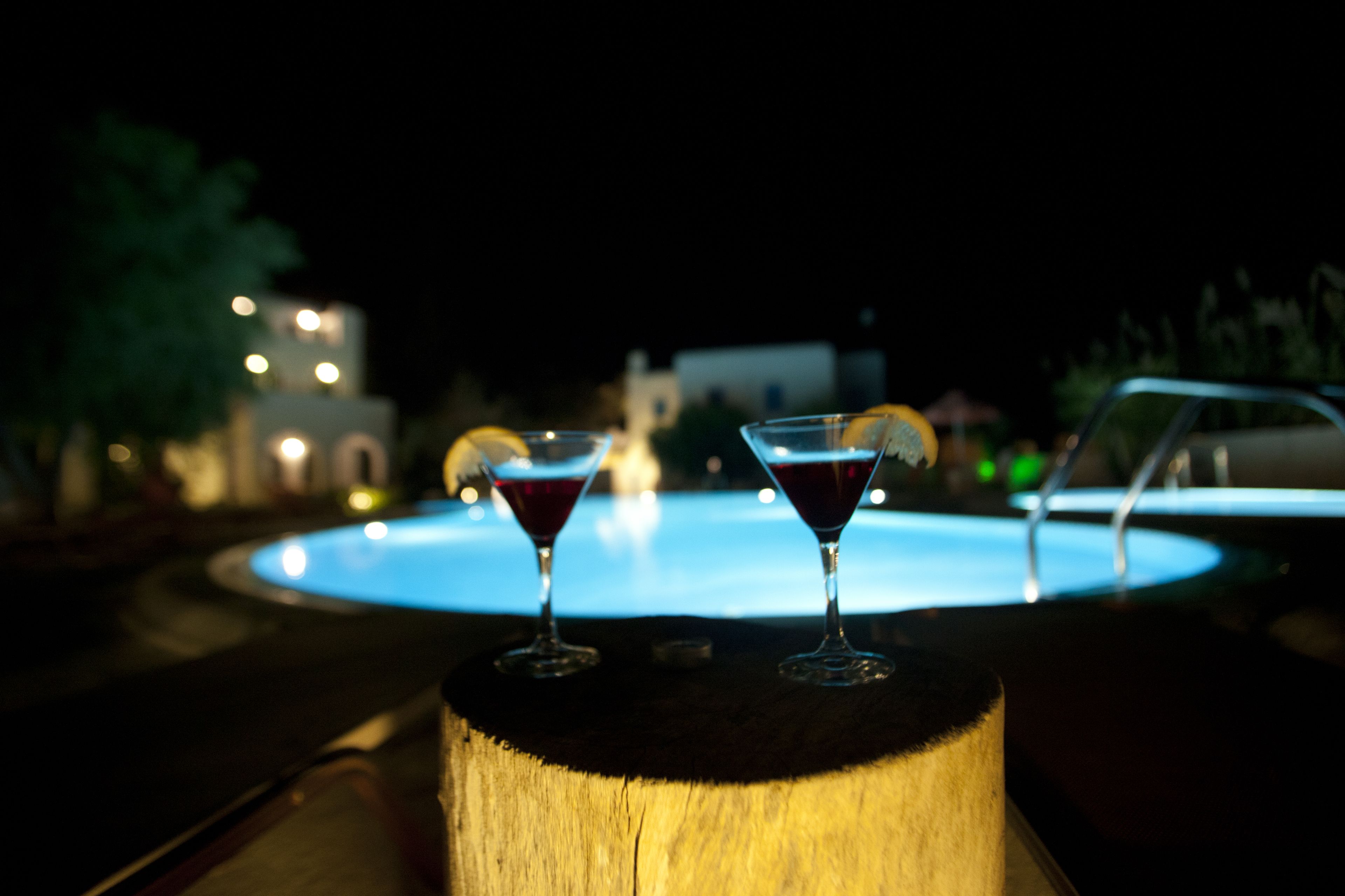 Dos vasos de martini sobre una superficie de madera, con una piscina al fondo.