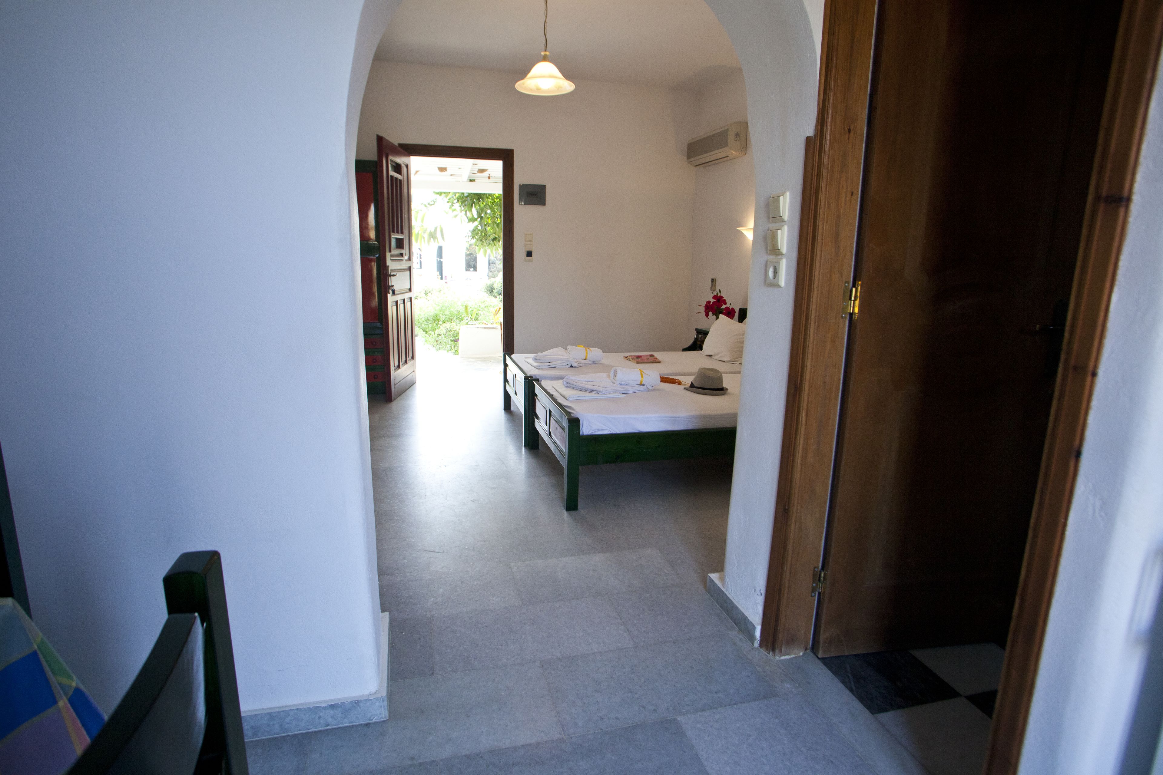 A narrow hallway leading to a bedroom with a bed, bedside table, and a small window.