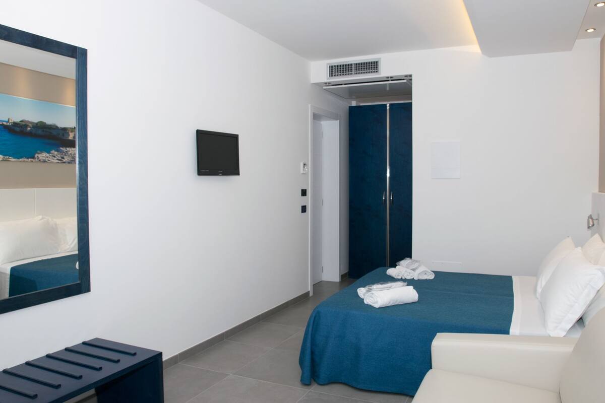 A modern hotel room with a large bed, a seating area, a television, and a wardrobe.
