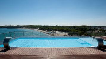 Ein Poolbereich mit Holzterrasse, mit Blick auf einen Strand und einen bewaldeten Bereich.
