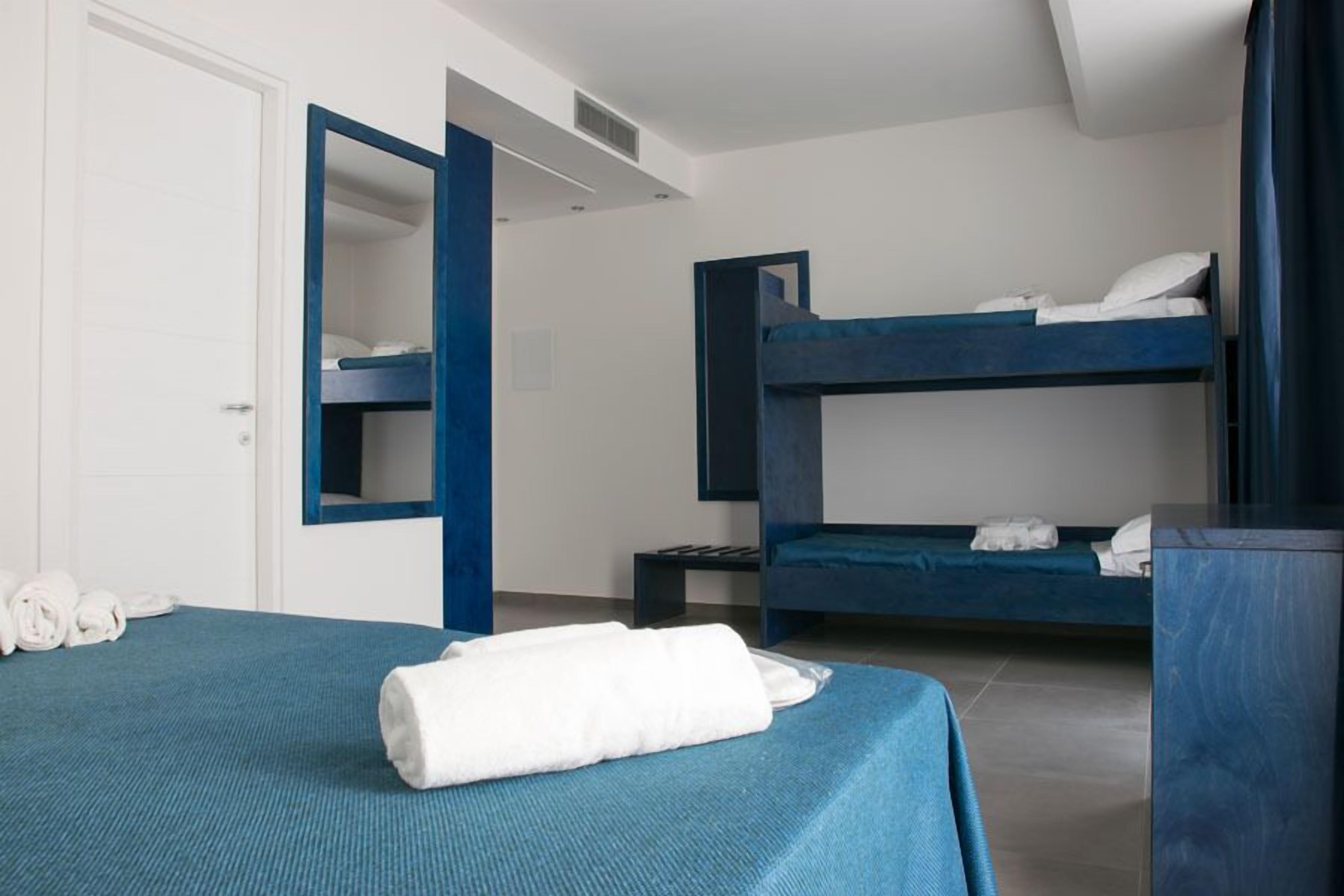 Une chambre d’hôtel avec un lit superposé, un bureau et un lit recouvert d’une couverture bleue.