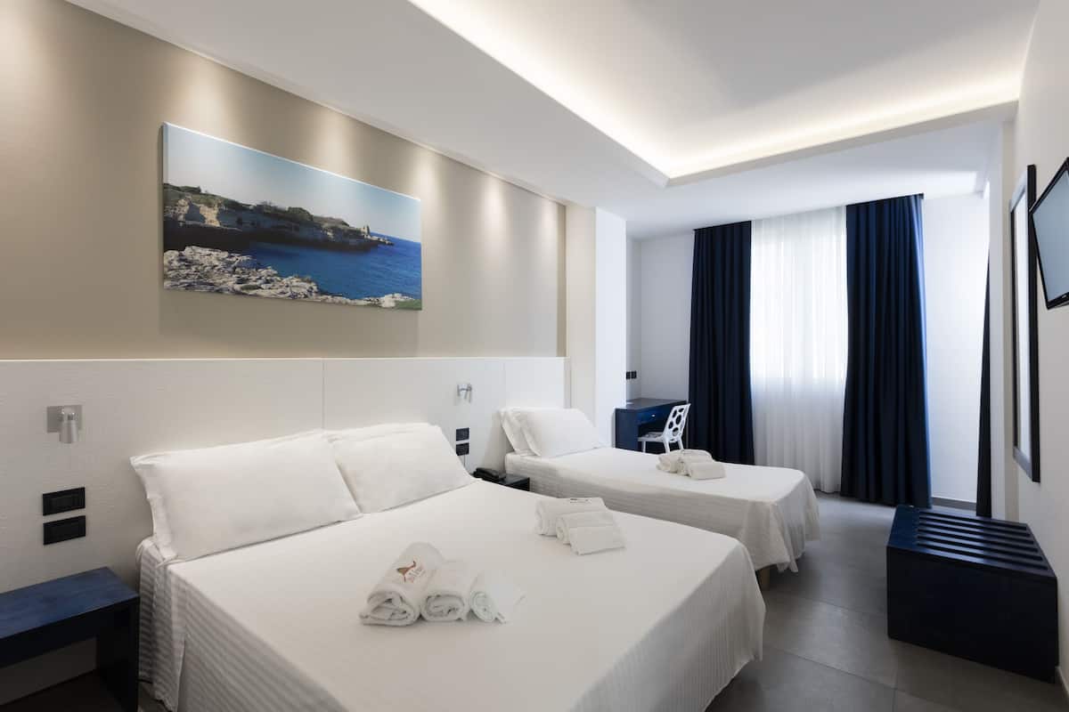 A hotel room with two beds, a desk, a chair, a painting, and a TV.