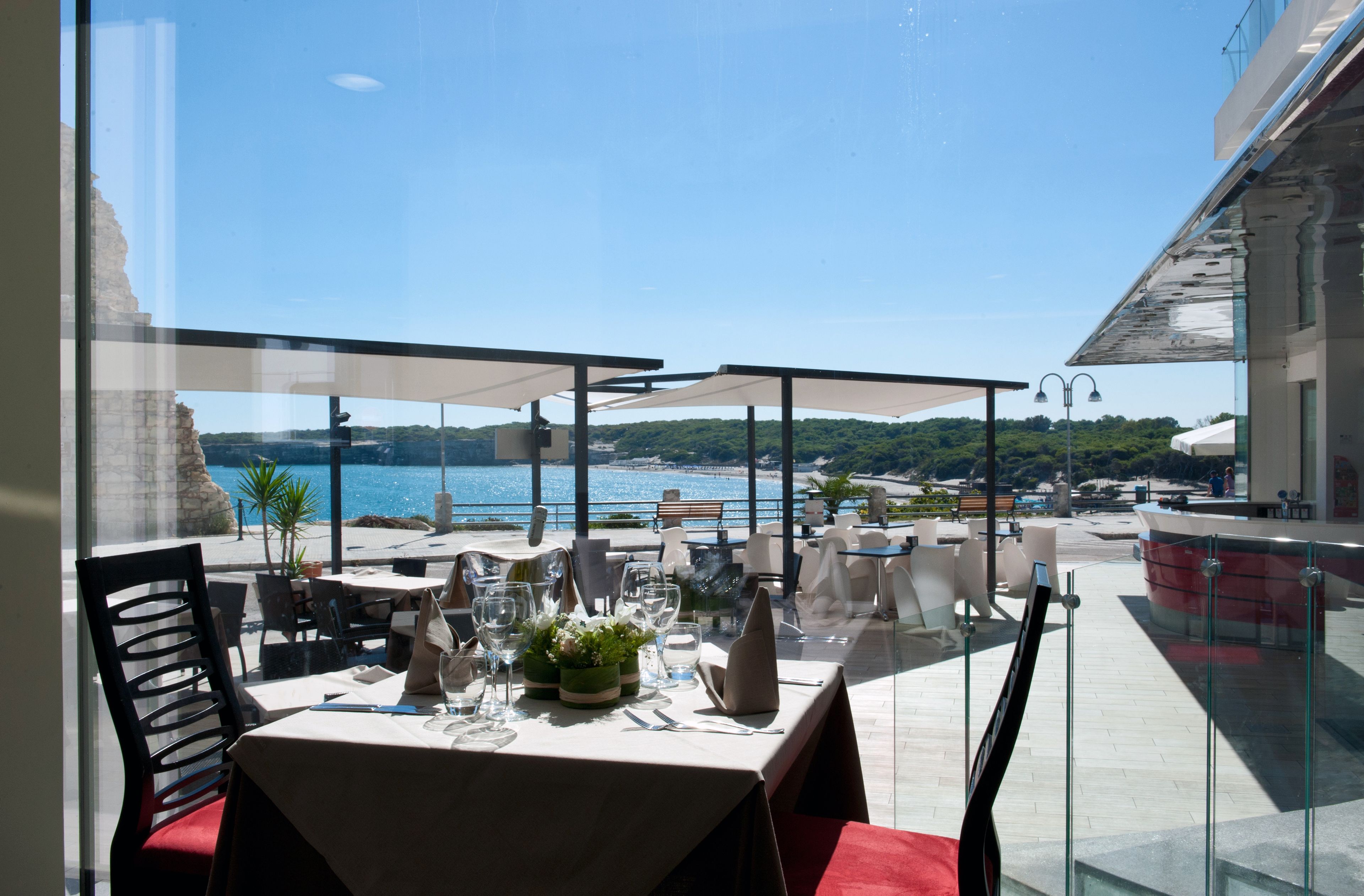 Un espace de restauration en plein air avec des tables disposées pour deux personnes, offrant une vue panoramique sur la côte.