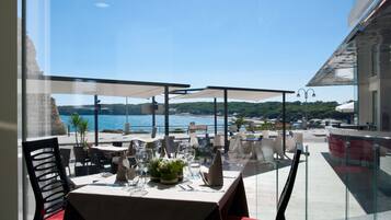Un espace de restauration en plein air avec des tables disposées pour deux personnes, offrant une vue panoramique sur la côte.