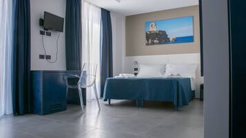 Una camera d'albergo con un letto, una scrivania, una sedia, una TV a parete e un quadro raffigurante una scena costiera.