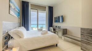 Een hotelkamer met een bed, een bureau, een televisie en uitzicht op zee.