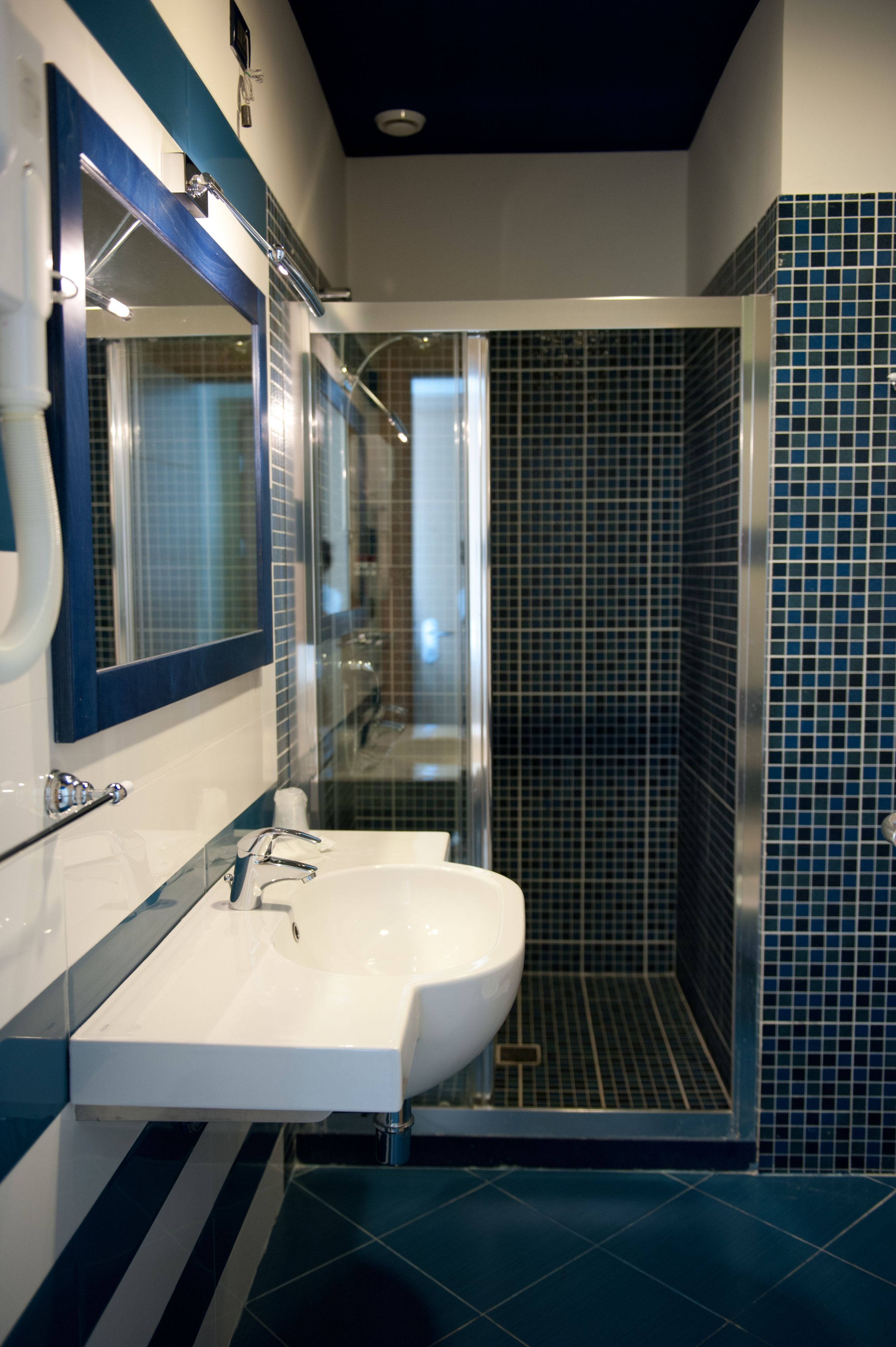 A modern bathroom with a white sink, a large mirror, and a glass-enclosed shower.