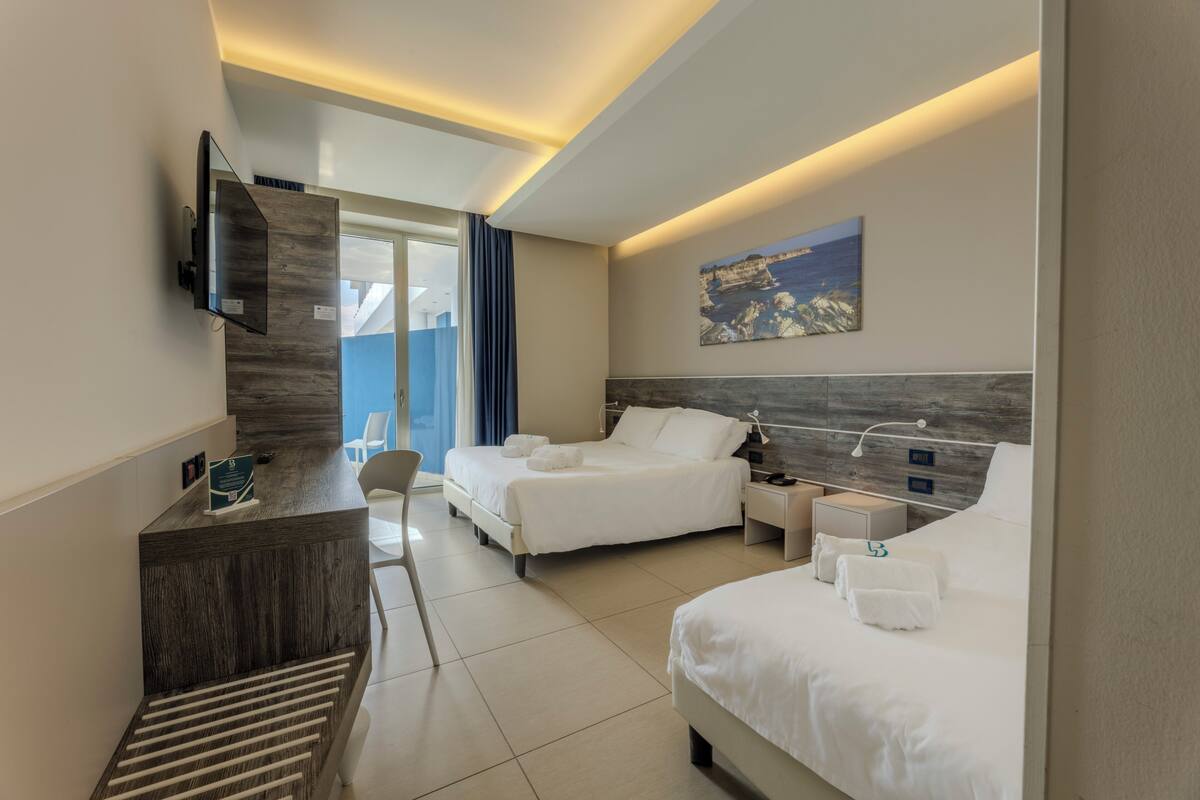 A hotel room with two beds, a desk, a TV, and a painting on the wall.