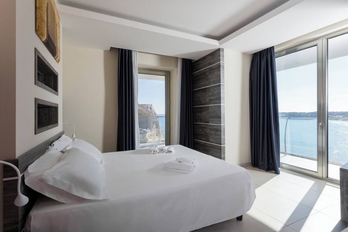 A hotel room with a large bed, a view of the sea, and a balcony.