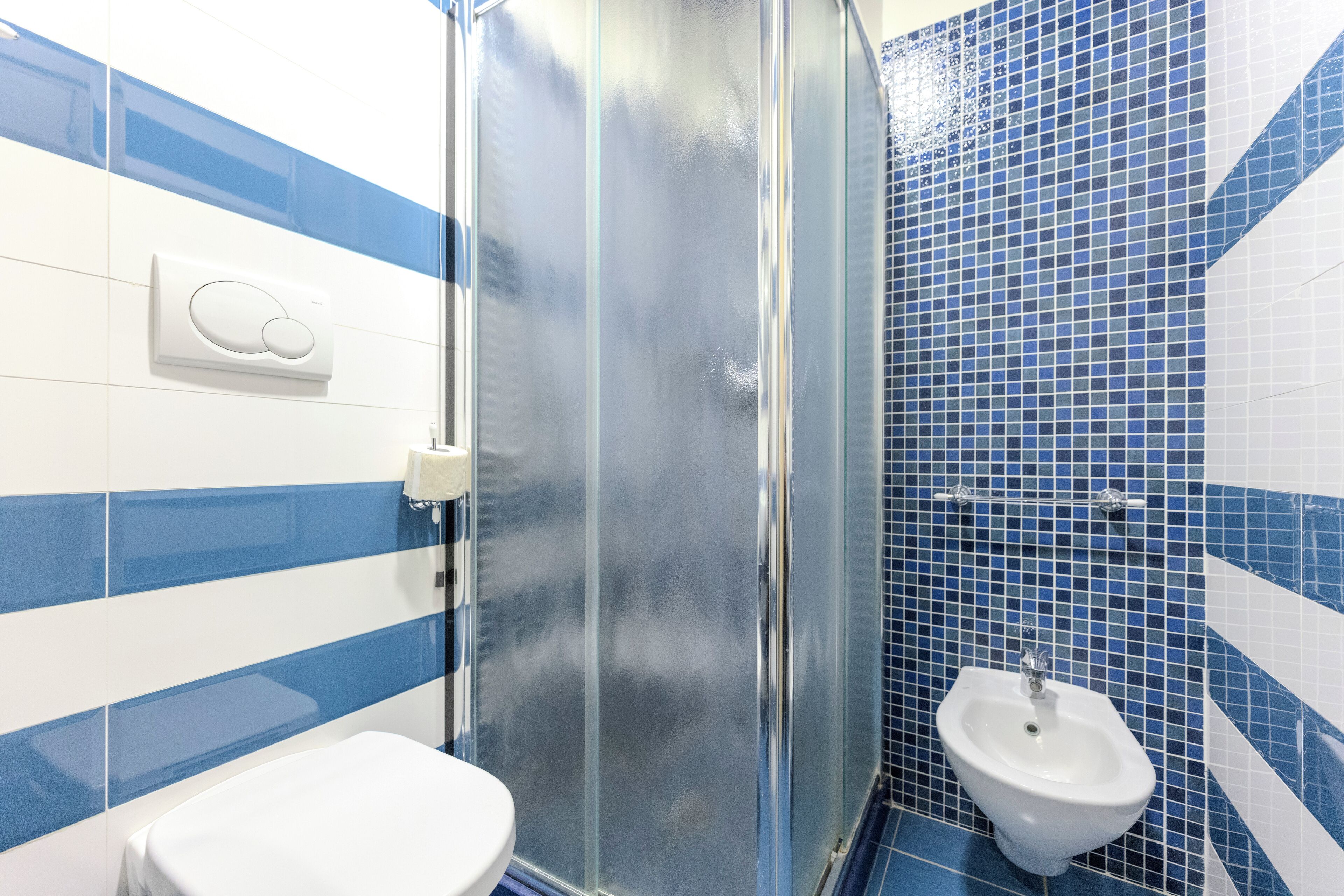 A bathroom with a glass shower enclosure, a toilet, and a bidet.