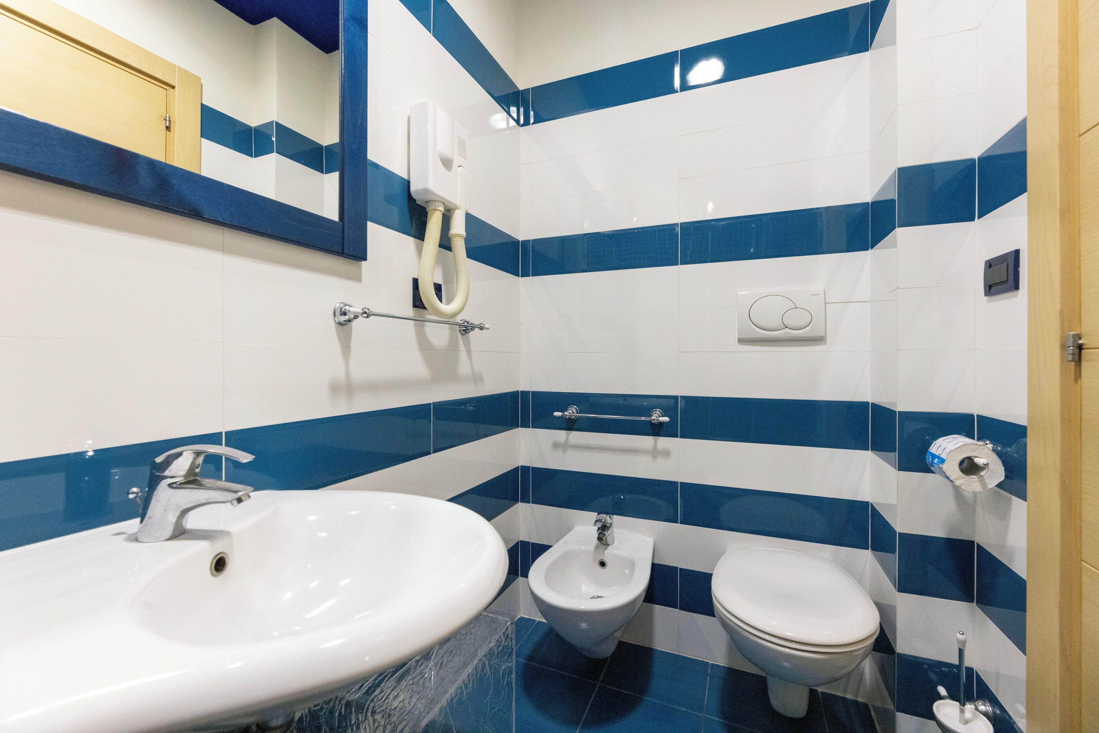 A bathroom with a sink, bidet, and toilet, tiled in blue and white.