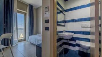 Ein Hotelzimmer mit Bett, Sessel, Bad mit Waschbecken und Toilette sowie Blick auf die Stadt durch das Fenster.