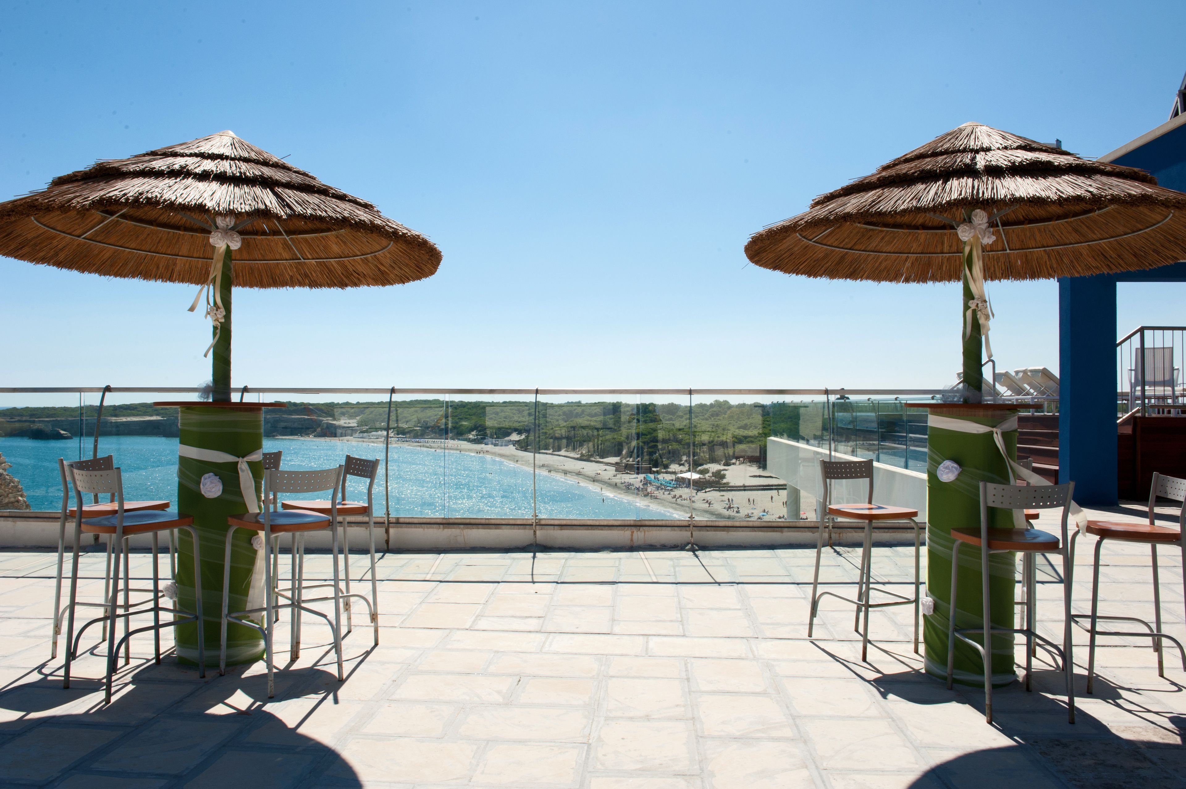Eine Terrasse mit zwei Strohdächern, Stühlen und Blick auf Strand und Meer.