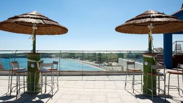 Eine Terrasse mit zwei Strohdächern, Stühlen und Blick auf Strand und Meer.