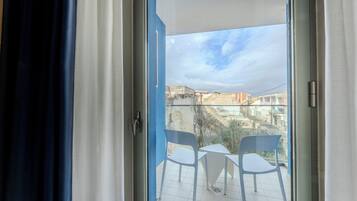 Een balkon met twee witte stoelen en een kleine tafel, met uitzicht op een stadslandschap met gebouwen en een heldere lucht.
