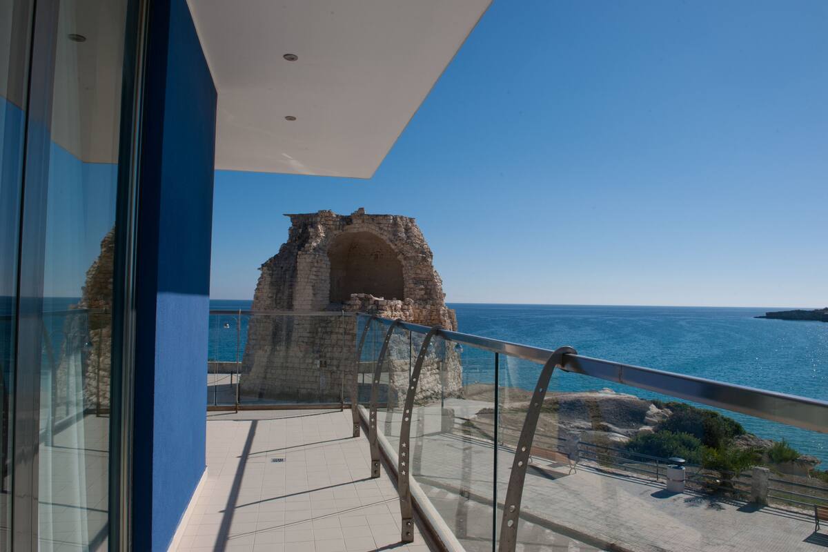 A balcony with a clear view of the sea and a stone structure.