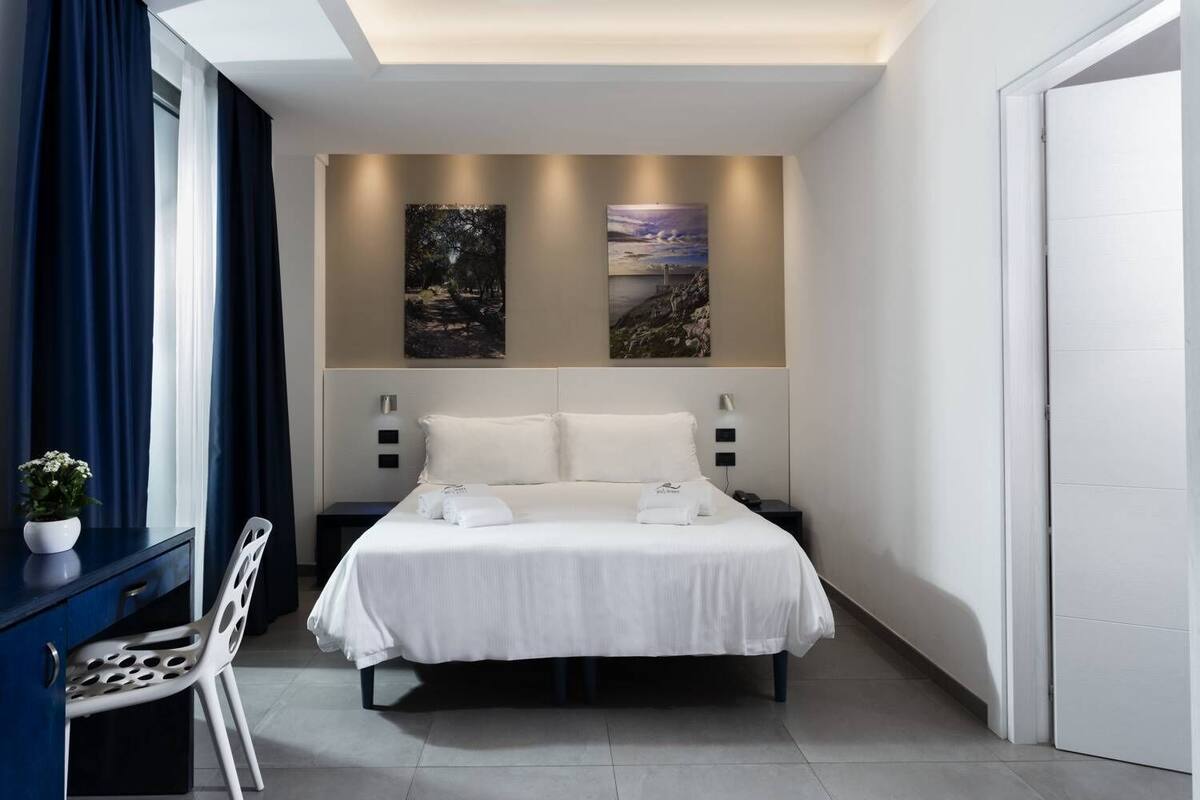 A modern bedroom with a bed, two wall-mounted lights, and two paintings.