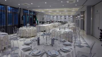 Un salón de banquetes con mesas redondas dispuestas para comer, sillas transparentes y piso a cuadros.