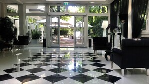 A lobby with a black and white checkered floor, a reception desk, and large windows with outdoor seating visible. - Boutique Hotel Calzavecchio (Casalecchio di Reno)