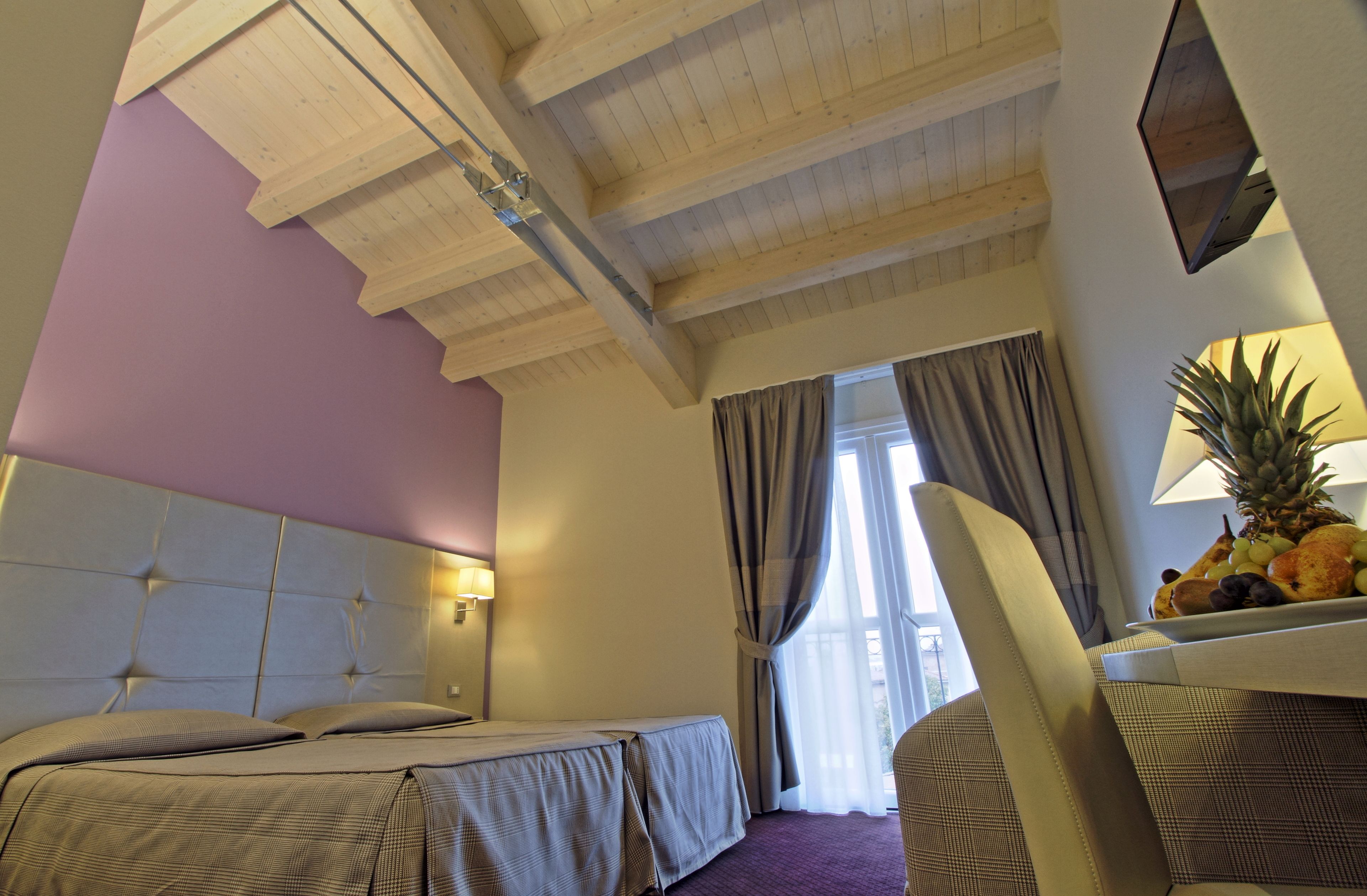 Una camera d'albergo con un letto, una sedia, una ciotola di frutta su un tavolo e una finestra con tende.