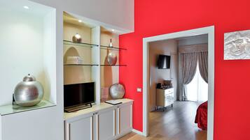 Una sala de estar moderna con una pared de acento roja, un televisor de pantalla plana y un aparador de vidrio con objetos decorativos.