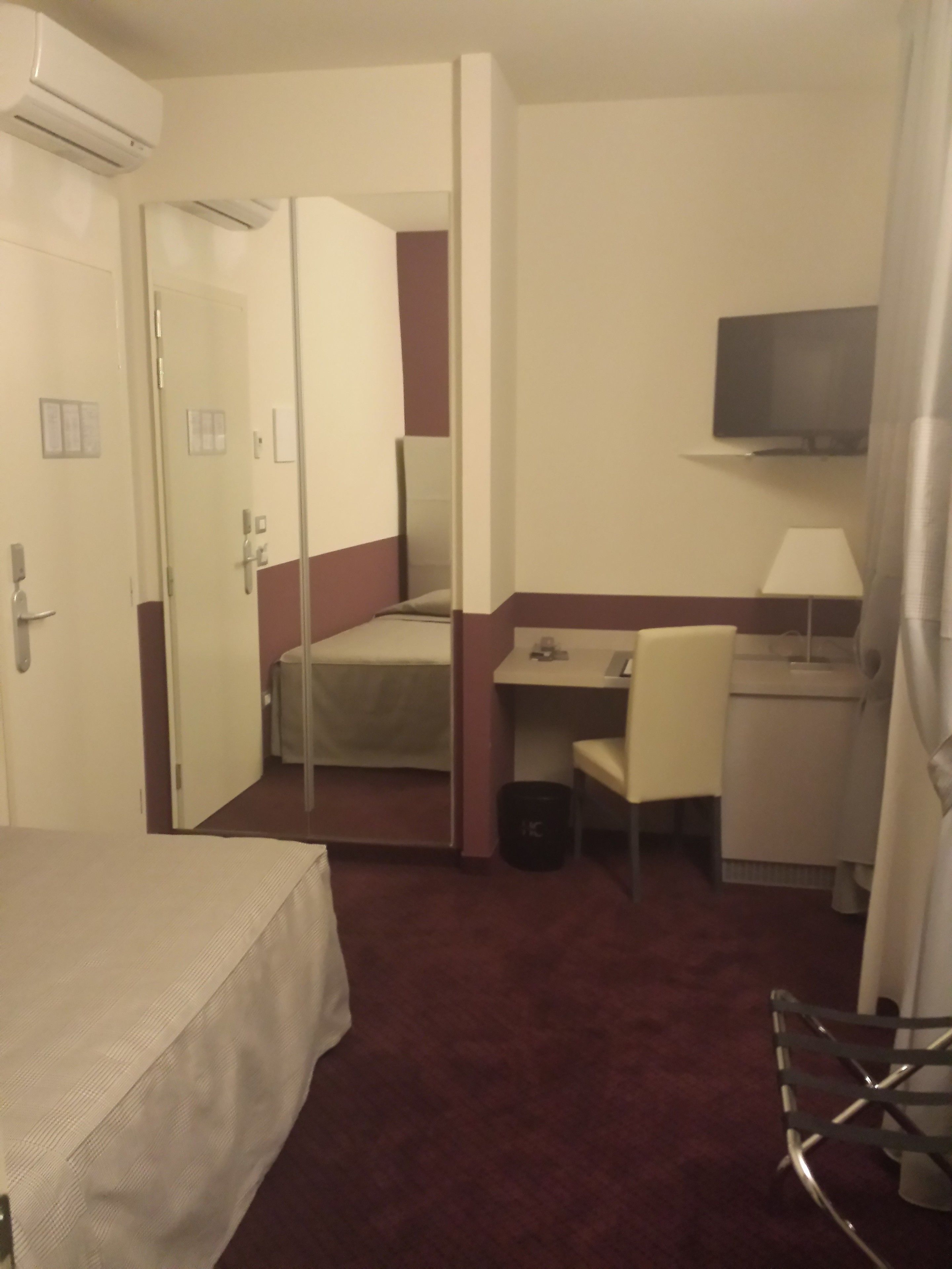 Une chambre d’hôtel avec un lit, un bureau, une chaise, une télévision et un miroir.