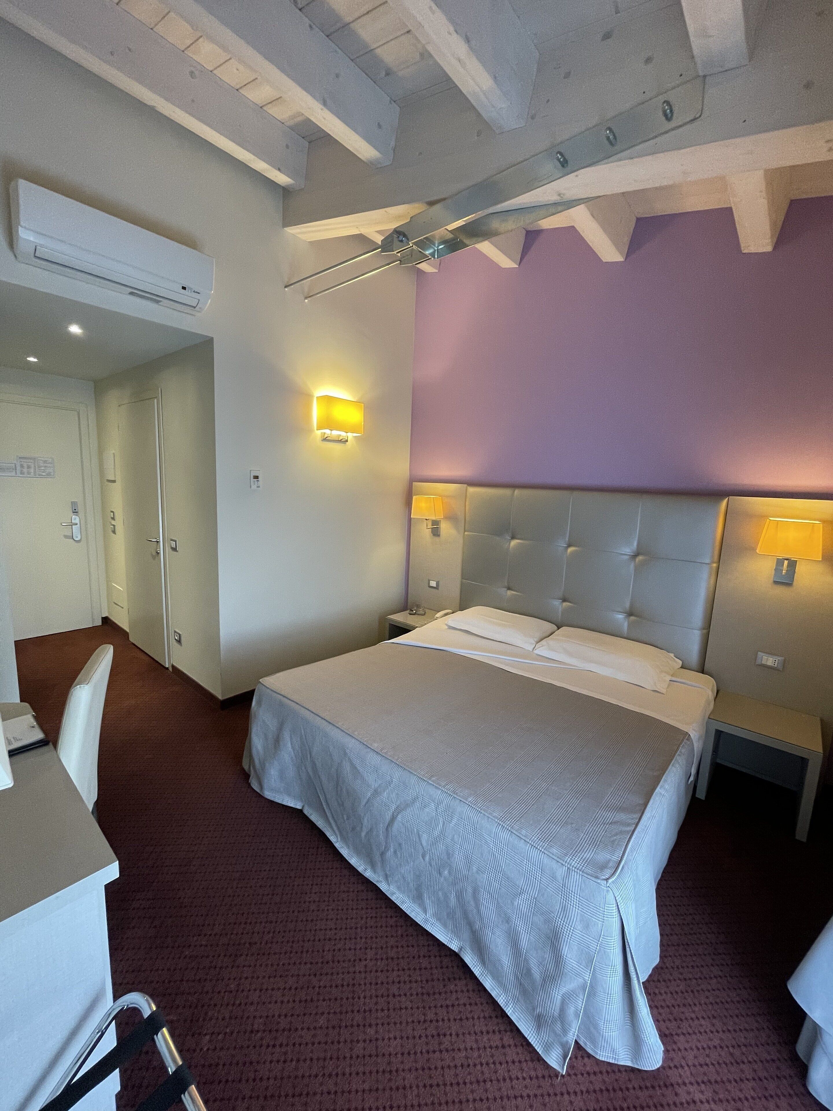 Una habitación de hotel con cama, mesitas de noche, escritorio y aire acondicionado.