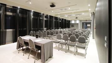 Ein Konferenzraum mit Reihen von Stühlen, einem Tisch mit Tischdecke und einem Projektor an der Decke.