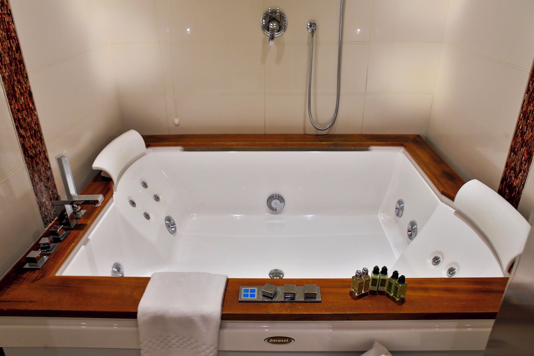 Een groot, rechthoekig bad met een houten omlijsting, een ingebouwd bedieningspaneel en een handdouche.